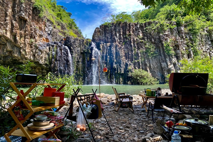 A riverside camping and BBQ setup with the stunning Vuc Hom Waterfall as the backdrop 