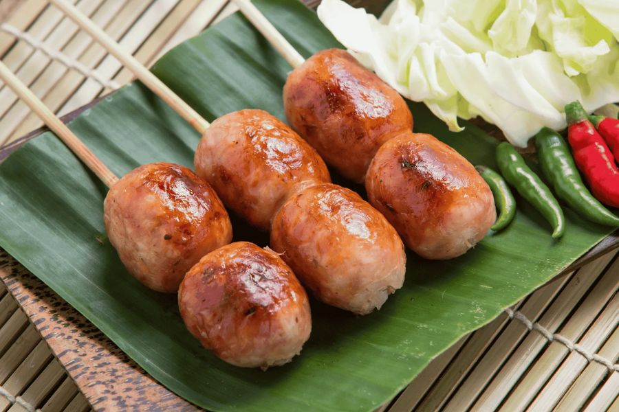 Grilled Sai Krok Isan (Isan-style fermented pork sausage) served with fresh chillies and cabbage
