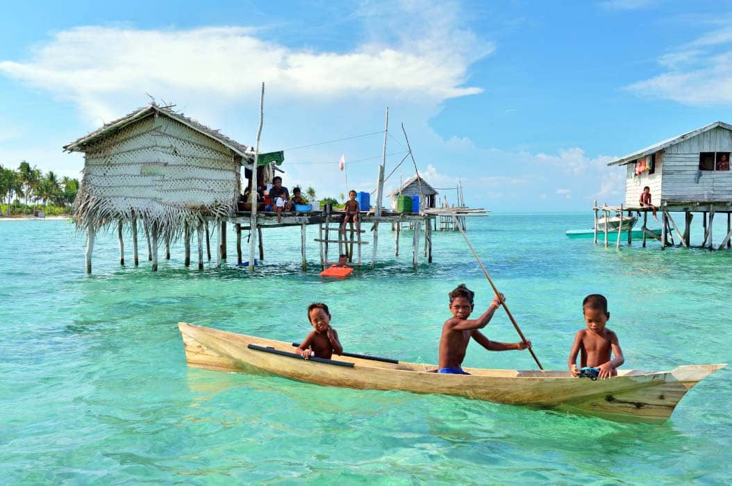 Three children are having fun rowing a boat around a fishing village in Mabul