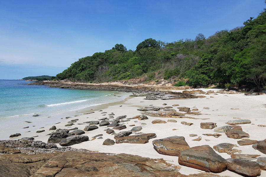 The beach is surrounded by lush greenery and rocky cliffs, providing a more secluded and intimate atmosphere