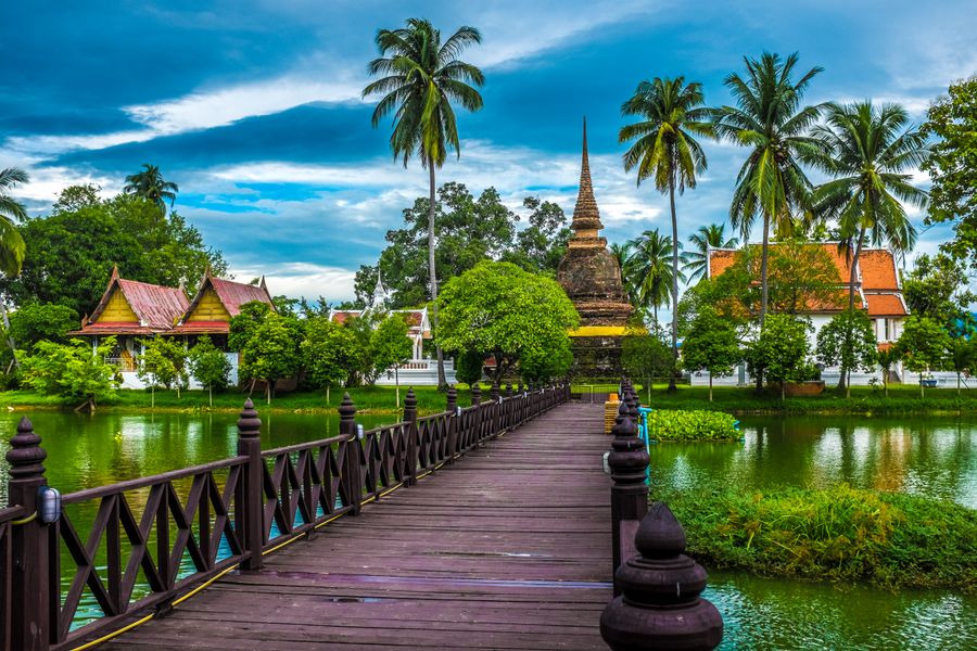 Discover the serene beauty of the Sukhothai temple, surrounded by lush greenery and tranquil waters.