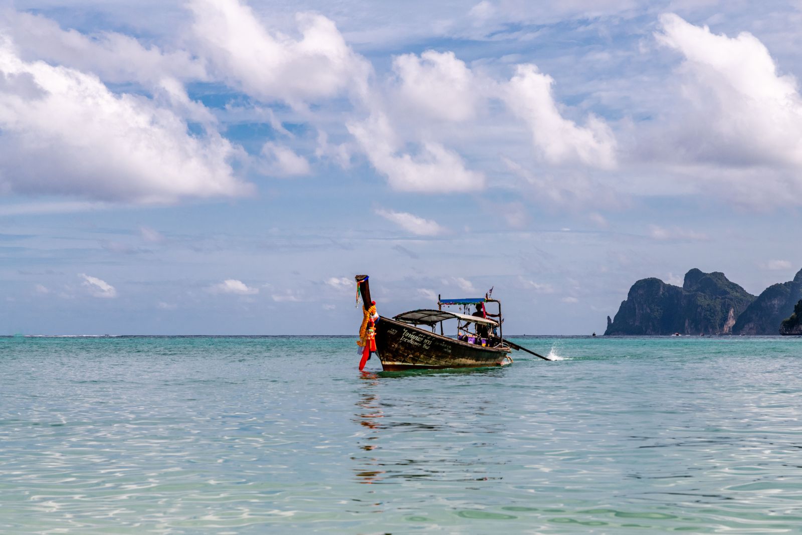 Discover a peaceful scene aboard a traditional fishing boat off the coast of Phuket, featuring calm waters and a cloudy sky.