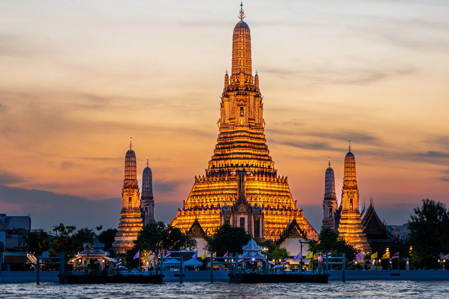 The captivating sight of Wat Arun illuminated at sunset along the banks of the Bangkok river