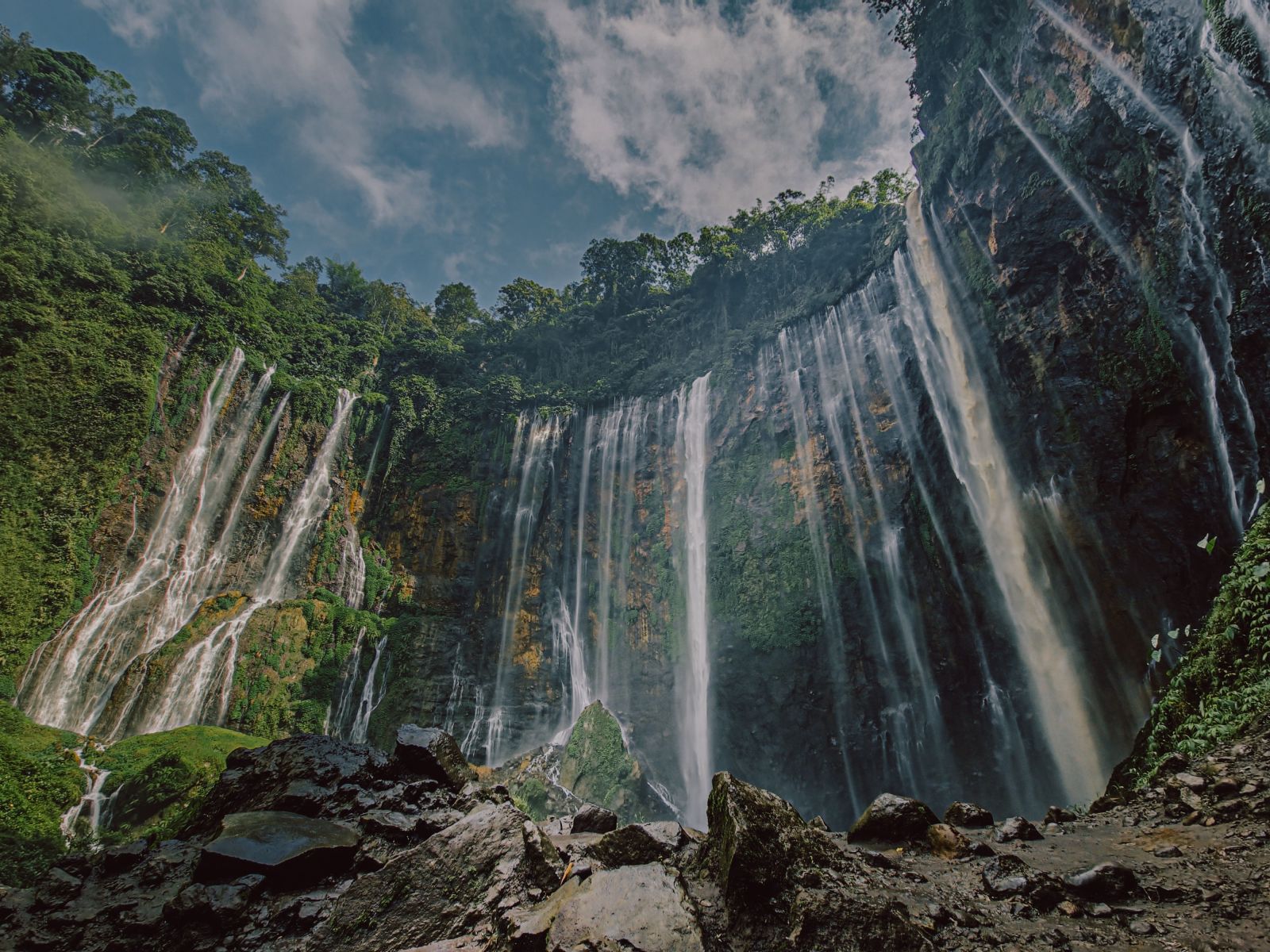 A stunning view of a majestic waterfall cascading down amidst a lush green forest under a bright blue sky