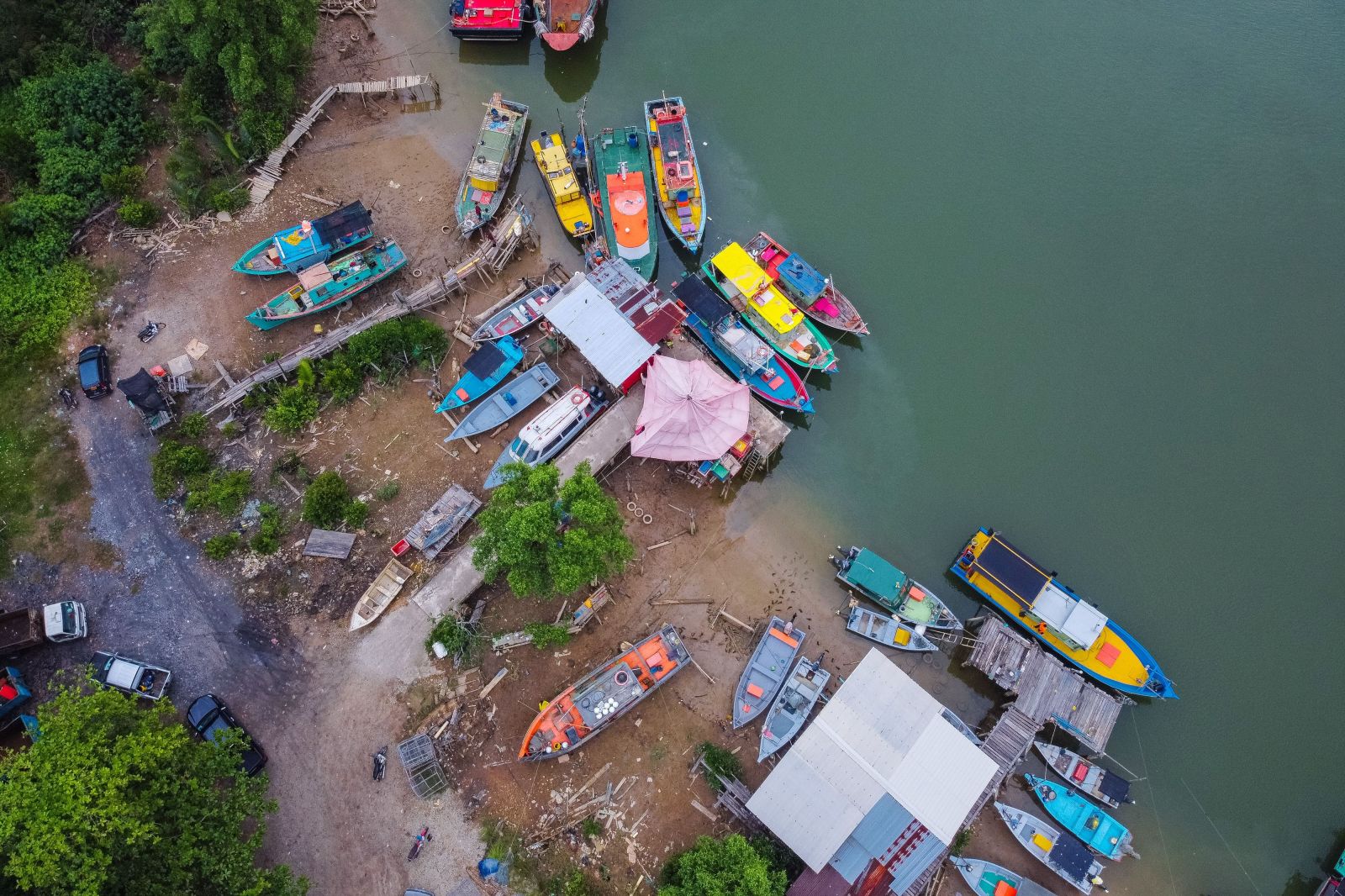 An aerial view of colorful boats moored along the riverbank in Chukai, Malaysia, amidst lush green vegetation.