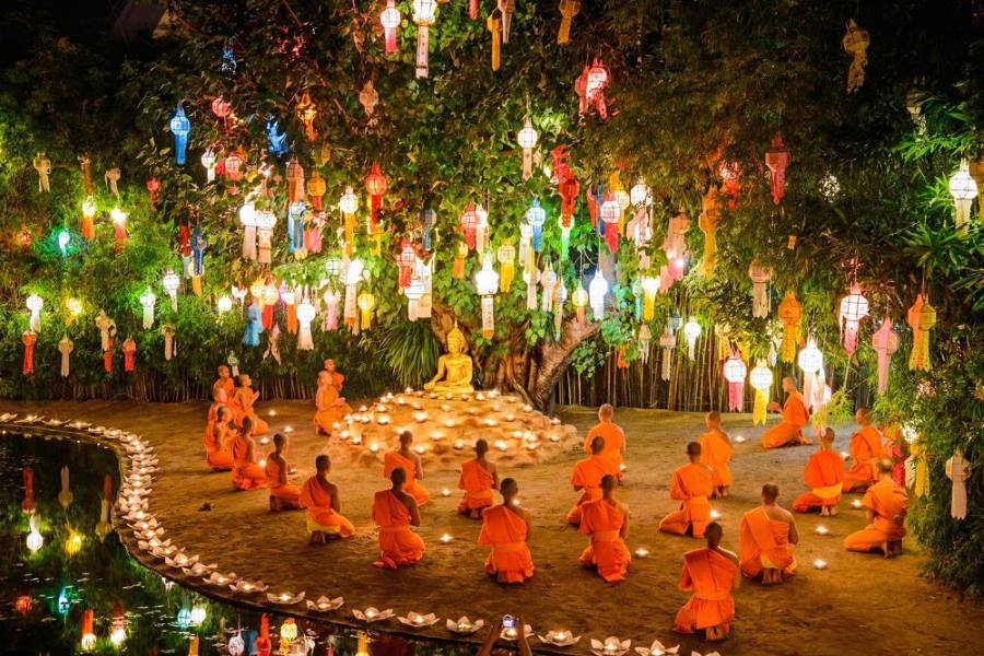 Monks gathered under a tree adorned with colorful lanterns during Yi Peng Festival in Chiang Mai